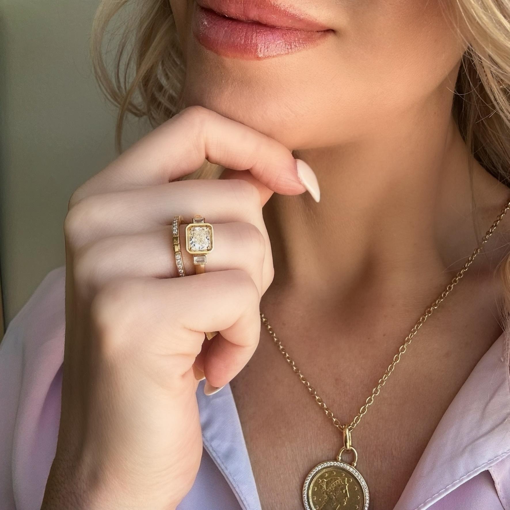 lifestyle image of woman wearing our Aubri 18k Yellow Gold Bezel Set Cushion Diamond & Baguette Three Stone Ring