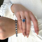 18k Yellow Gold Cushion Cut Sapphire & Trapezoid Diamond Three Stone Ring on hand with matching tennis bracelet